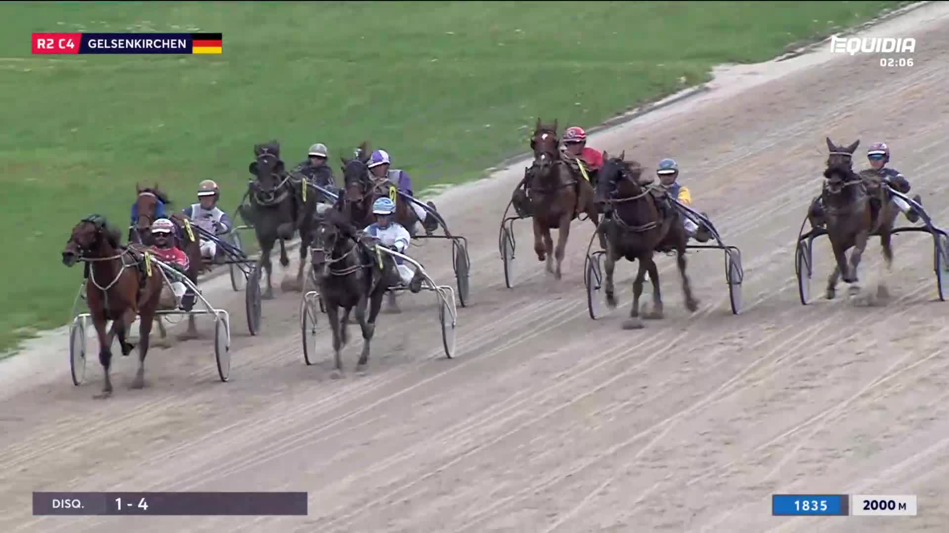 Harness horses, each pulling a sulky, thunder down the track. The jockeys, wearing brightly colored silks, urge their steeds forward.

