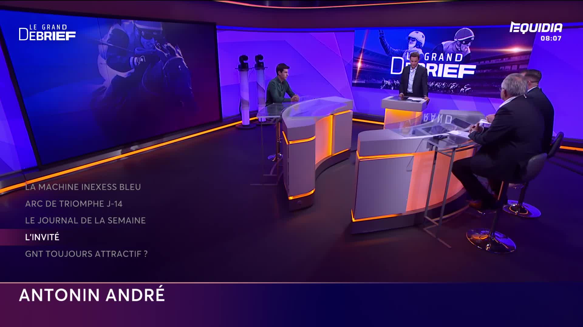 On the Equidia set, three men in suits are seated at a curved desk, while another stands at a podium. The backdrop shows a racing scene, and the show's title, "Le Grand Débrief," is prominently displayed.
