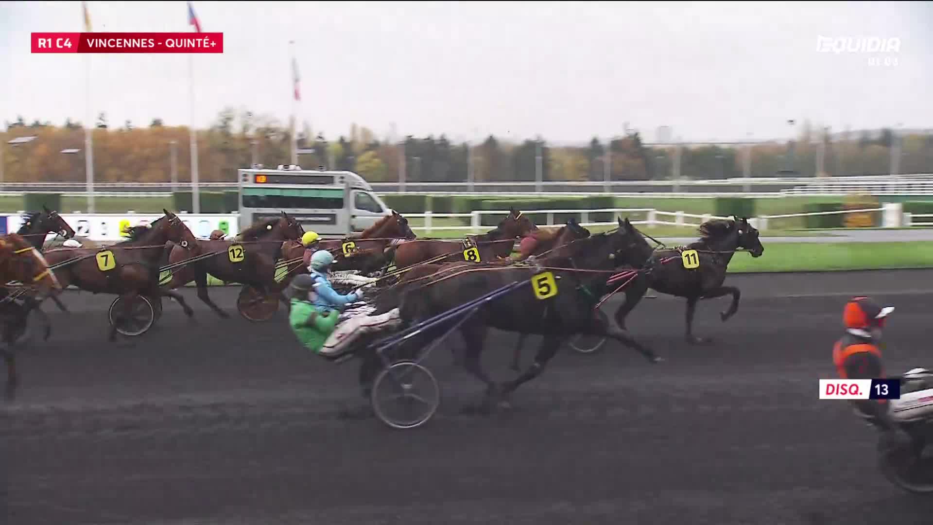 Harness horses, their drivers crouched low, are thundering around the track at Vincennes. Number 5, with the black coat, is leading the pack.
