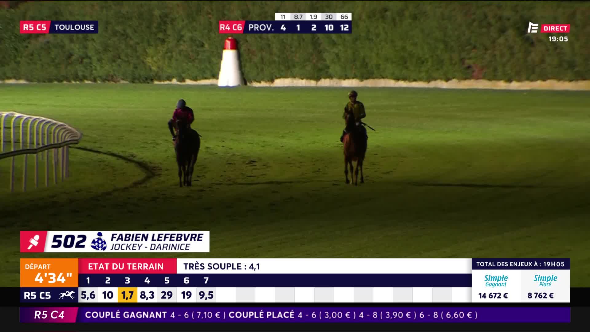 Two riders, each astride a horse, are making their way across the track. The horses are walking, with the jockeys in full riding gear.
