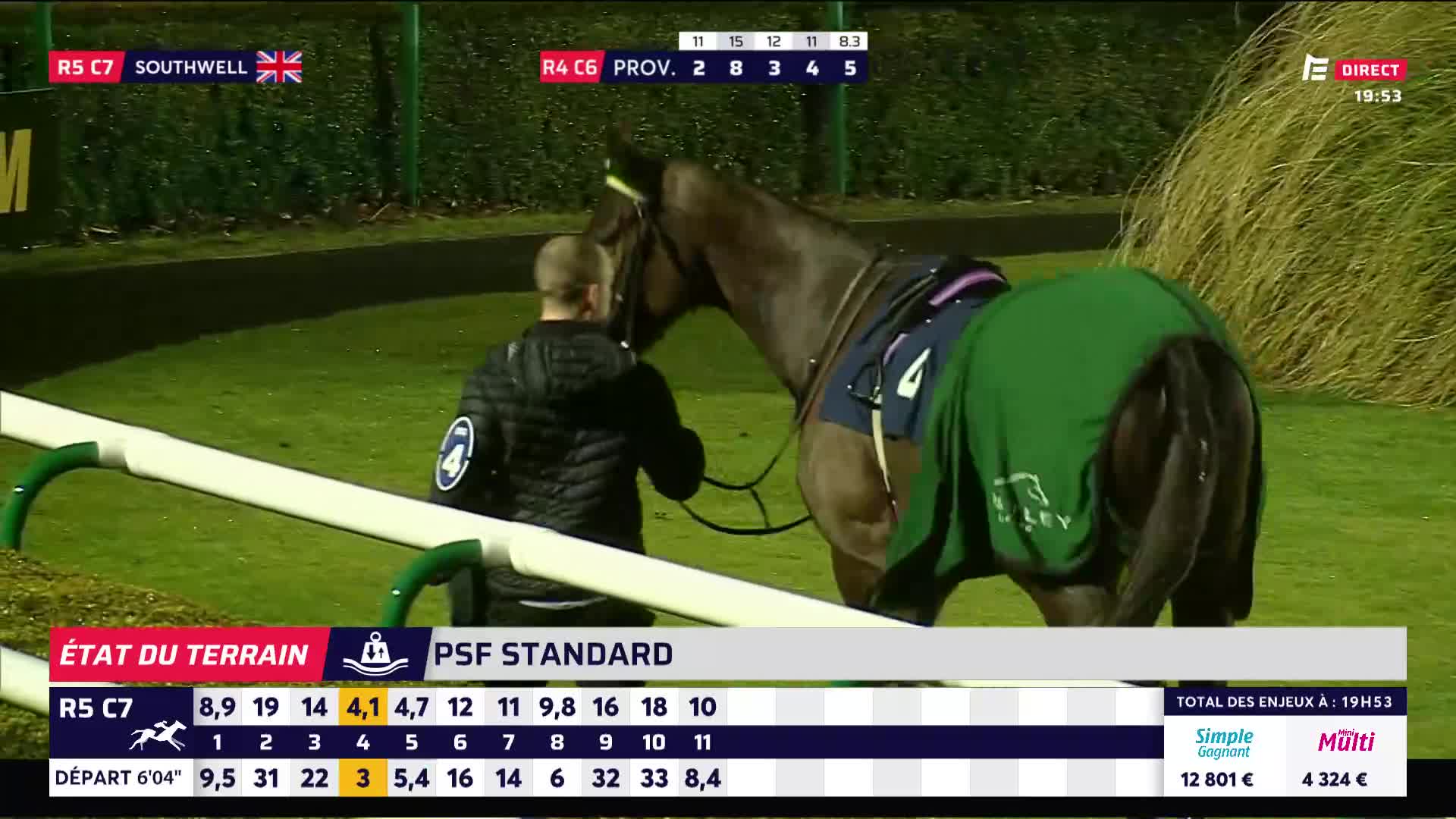 A handler leads a dark bay horse, draped in a green blanket, across the grass. The horse's saddlecloth displays the number 4.