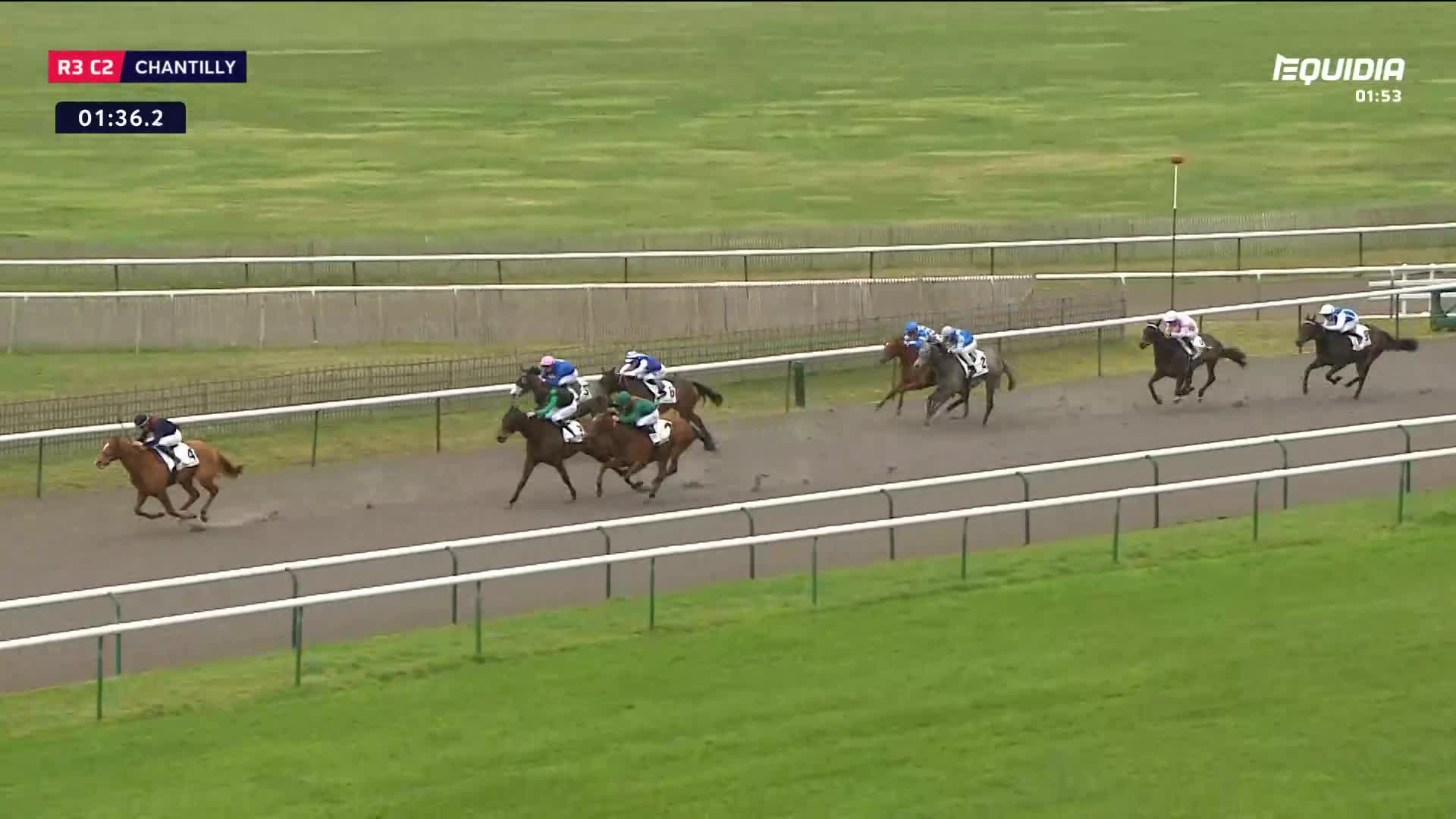 The horses are thundering down the track at Chantilly, jostling for position. A jockey in green and white urges his mount forward, gaining on the leaders.