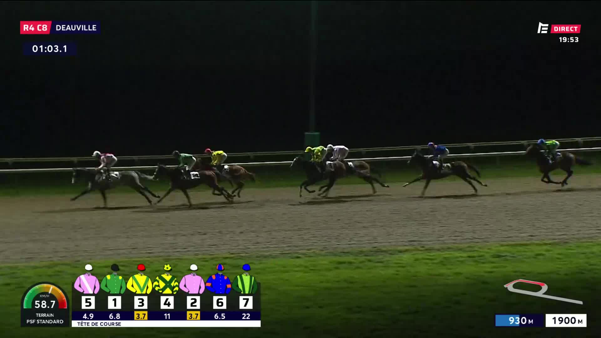 The horses are galloping down the track at Deauville. One jockey in pink and white is pulling ahead, while others in green, yellow, and blue are close behind.