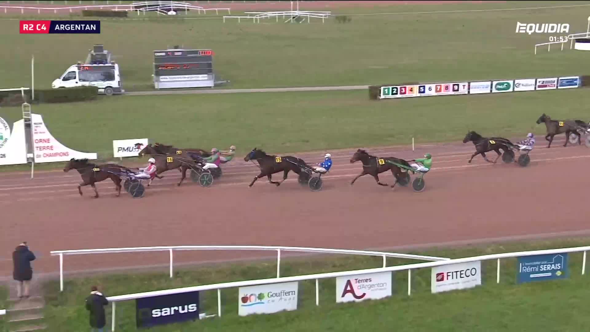 The horses are thundering down the track at Argentan, their sulkies kicking up dust. A driver in green and white is pushing hard, just ahead of a competitor in blue.