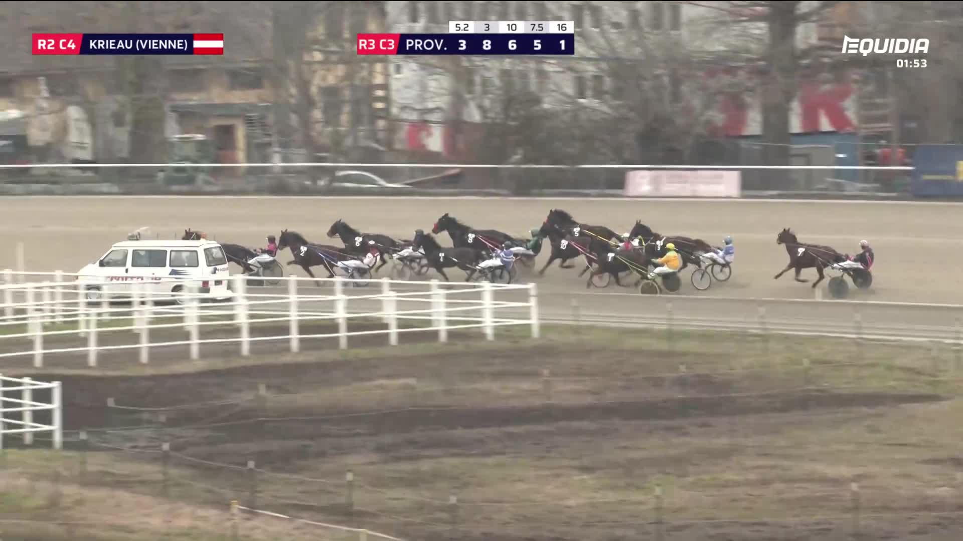 A pack of horses pulls sulkies down the track, jostling for position. One horse pulls slightly ahead, its driver focused on the finish line.