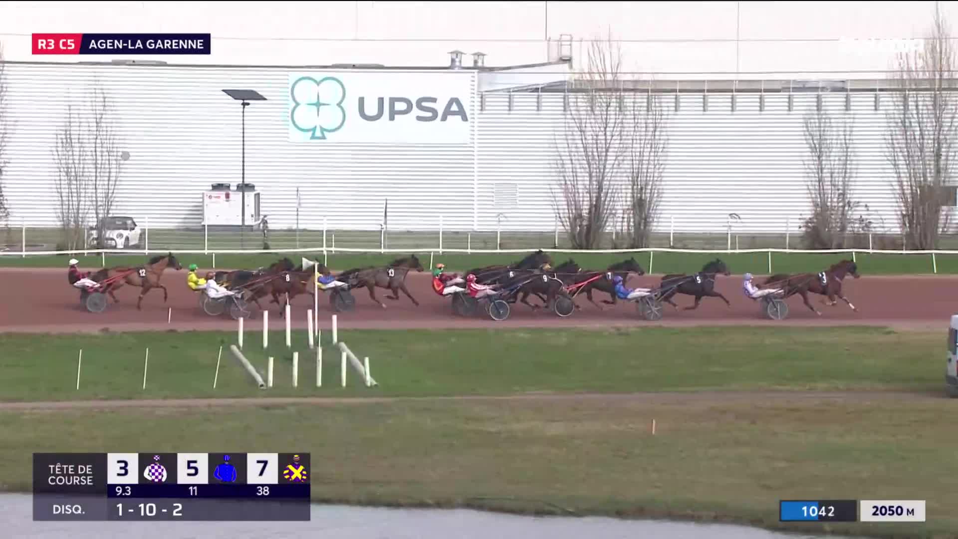 The horses are pulling their sulkies around the turn, jostling for position.  The number 3 horse is leading the pack, its driver leaning forward.