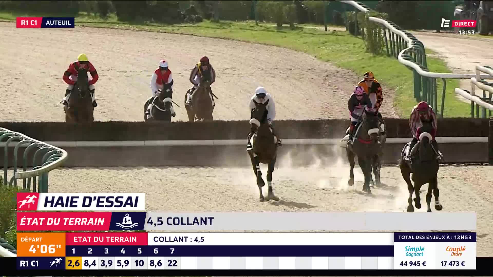 The horses are jumping the hurdle, kicking up dust on the sandy track. A jockey in white and black is leading the pack, his mount's legs extended mid-air. The horses are jumping the hurdle, kicking up dust on the sandy track. A jockey in white and black is leading the pack, his mount's legs extended mid-air.