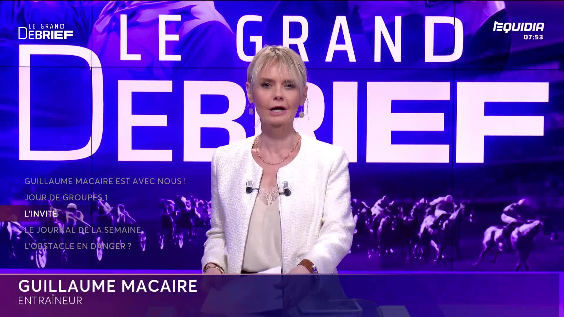 A woman in a white jacket speaks at a desk, her blonde hair framing her face. Behind her, a graphic displays "LE GRAND DEBRIEF" with a live feed of horses in full gallop. A woman in a white jacket speaks at a desk, her blonde hair framing her face. Behind her, a graphic displays "LE GRAND DEBRIEF" with a live feed of horses in full gallop.