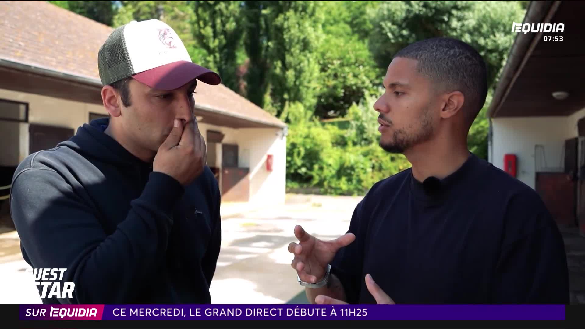 A man in a baseball cap gestures with his hand near his nose while talking to another man who is speaking animatedly. They stand outside a stable, with the Equidia logo visible on screen.