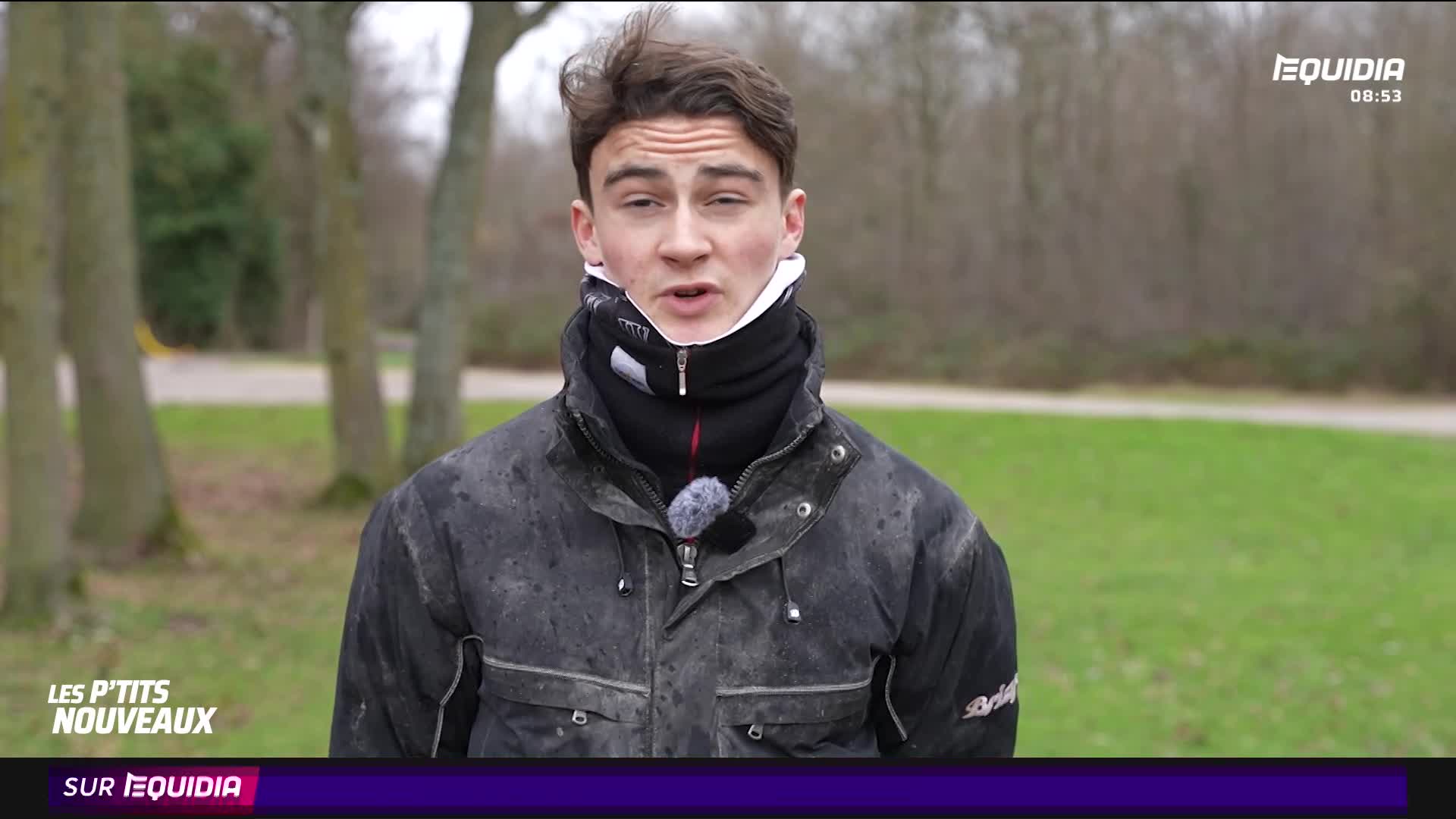 A young man stands outdoors, talking into a microphone attached to his jacket. He's bundled up in a thick, dark coat and a neck gaiter, likely for a segment on Equidia. A young man stands outdoors, talking into a microphone attached to his jacket. He's bundled up in a thick, dark coat and a neck gaiter, likely for a segment on Equidia.