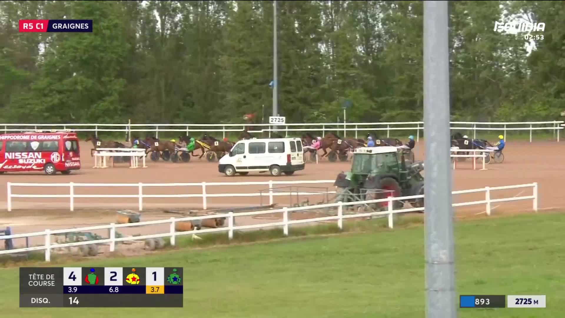The horses are thundering down the track at Graignes, their hooves kicking up dust. A green tractor slowly makes its way across the infield, its presence a stark contrast to the race unfolding.