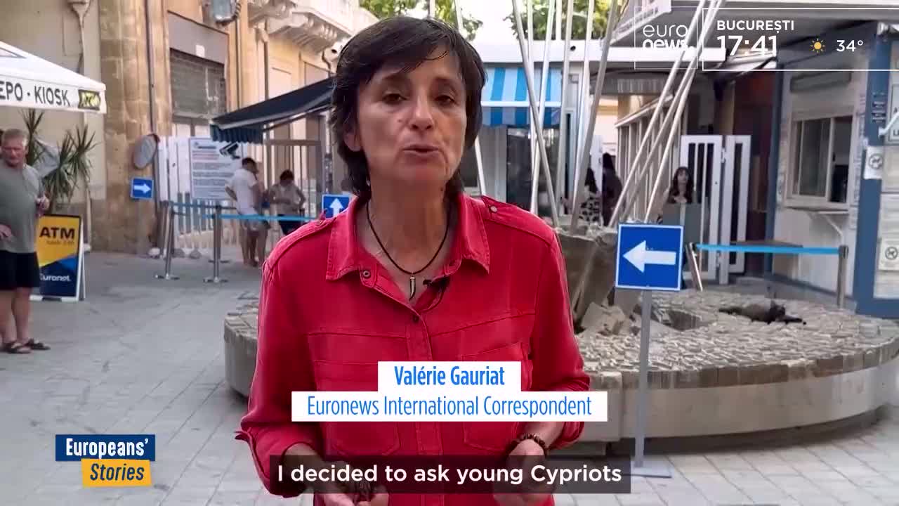 A woman in a red shirt speaks directly to the camera, a Euronews correspondent in Bucharest. Behind her, people mill about near a kiosk and a blue arrow sign points left.
