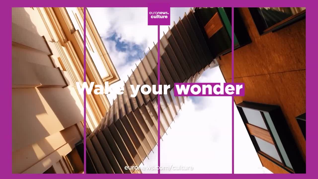 Looking up, I see a bridge-like structure connecting two buildings, framed by a clear sky. The Euronews English logo is visible, and the words "Wake your wonder" are prominently displayed.
