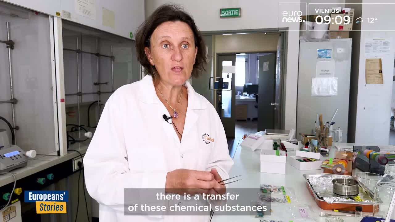 A woman in a lab coat, speaking on Euronews English from France, holds tweezers over a table cluttered with scientific equipment. The camera focuses on her as she explains the transfer of chemical substances.
