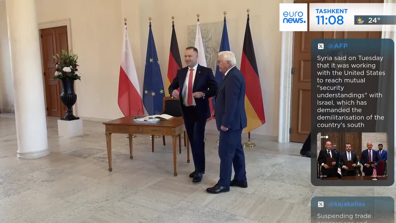 Two men in suits stand near a table, with flags of Poland, the EU, and Germany behind them. One adjusts his jacket while the other looks on, the scene likely from a Euronews report.
