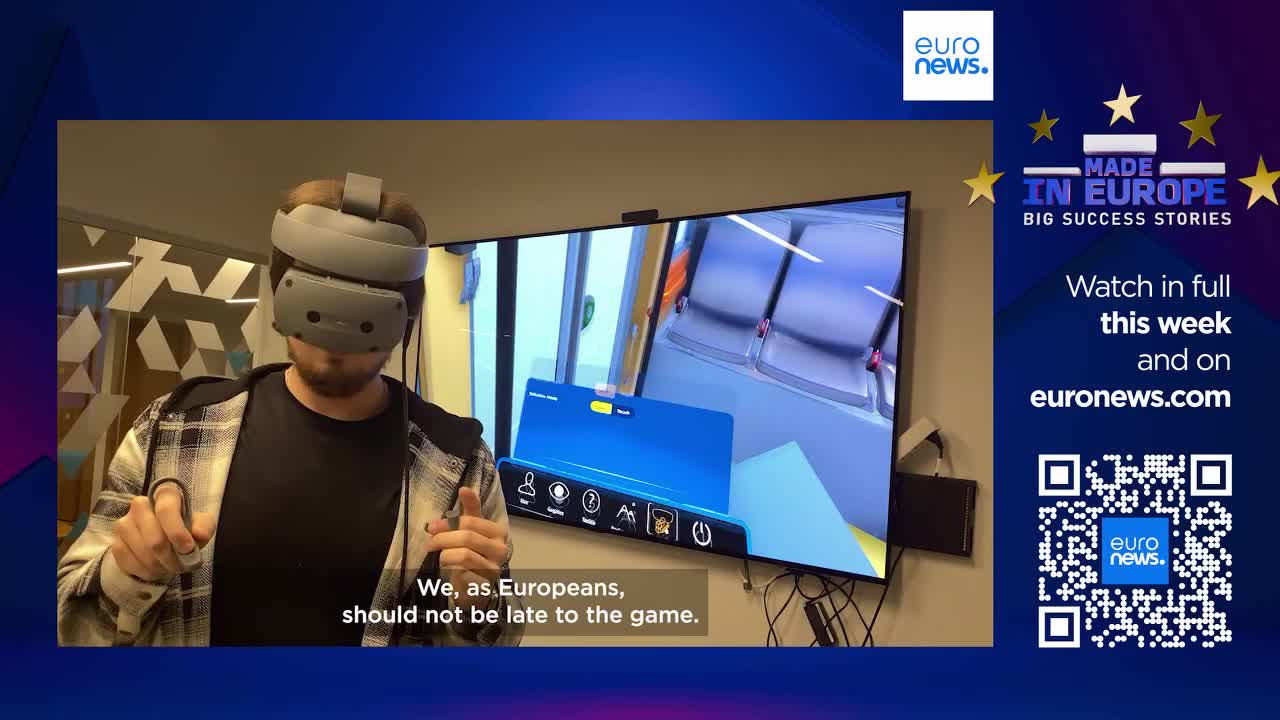 A man wears a VR headset, his hands holding controllers as he interacts with a virtual train carriage displayed on a large screen. The screen shows a digital representation of a train's interior, complete with seats and a control panel, as if viewed from within the carriage itself. A man wears a VR headset, his hands holding controllers as he interacts with a virtual train carriage displayed on a large screen. The screen shows a digital representation of a train's interior, complete with seats and a control panel, as if viewed from within the carriage itself.