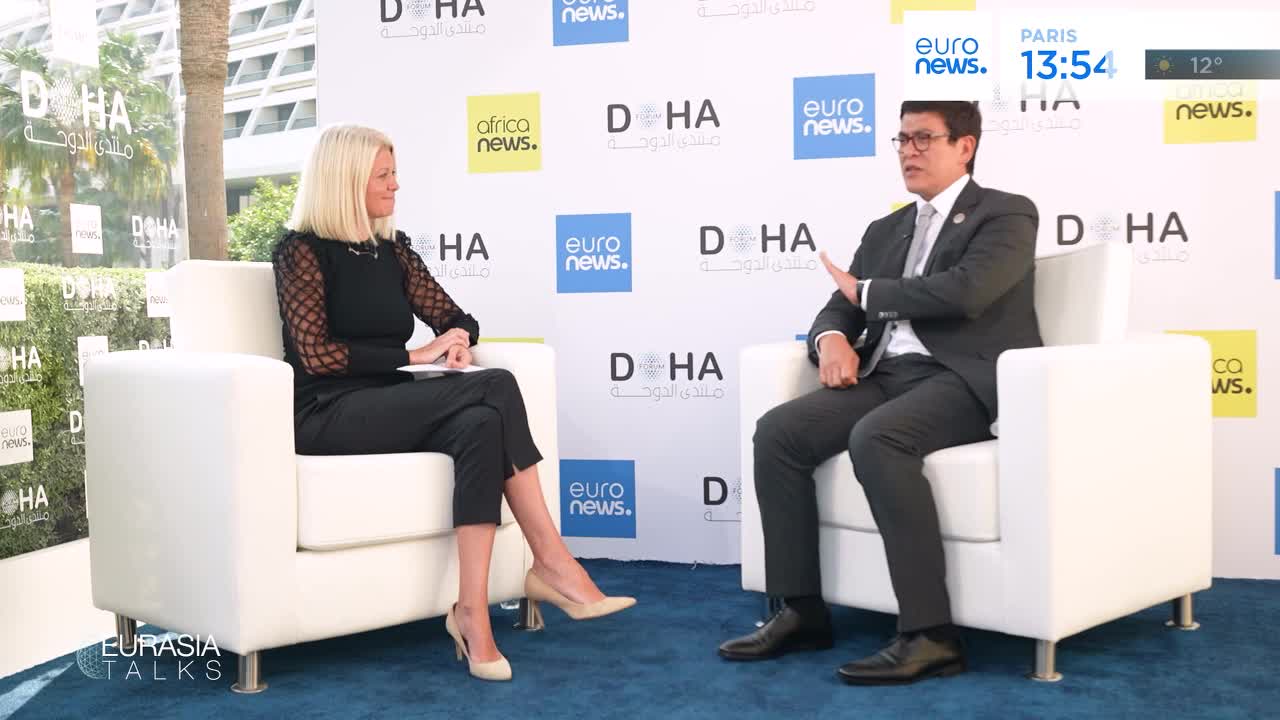 A man in a suit gestures with his left hand while seated opposite a woman in black. The backdrop displays "Doha" and "euronews."