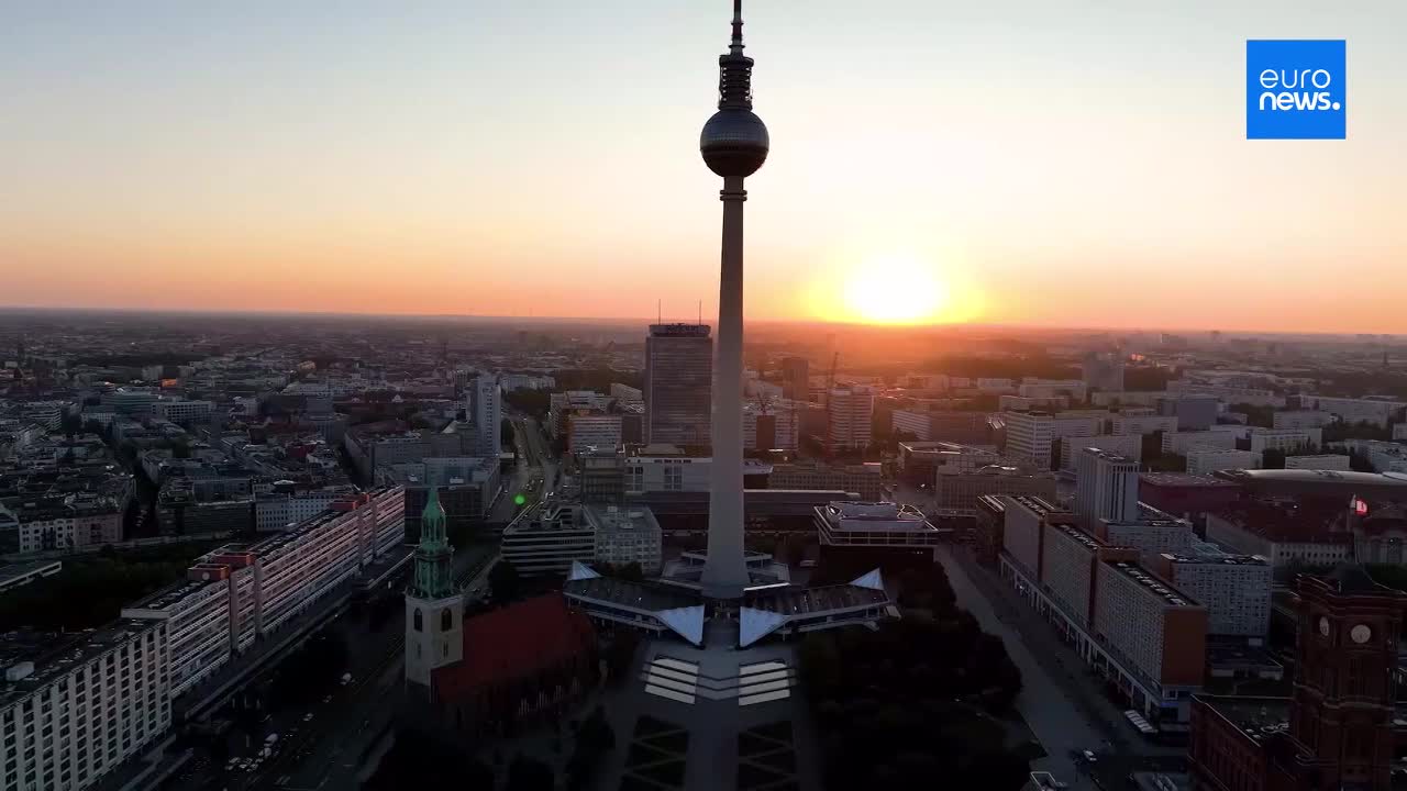 The sun dips below the horizon, casting a warm glow over the cityscape. A tall television tower dominates the view, its silhouette sharp against the fading light.