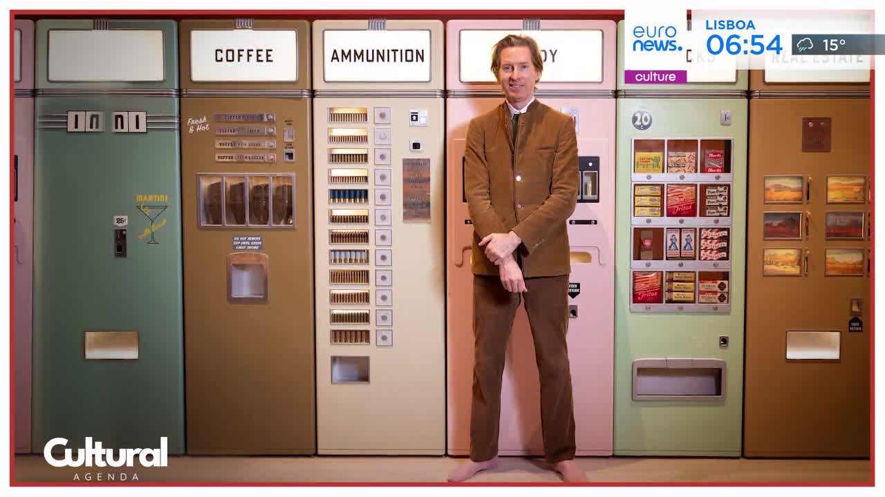 A man in a brown suit stands between rows of vintage vending machines. One machine is labeled "COFFEE," another "AMMUNITION," and a third displays small framed pictures.