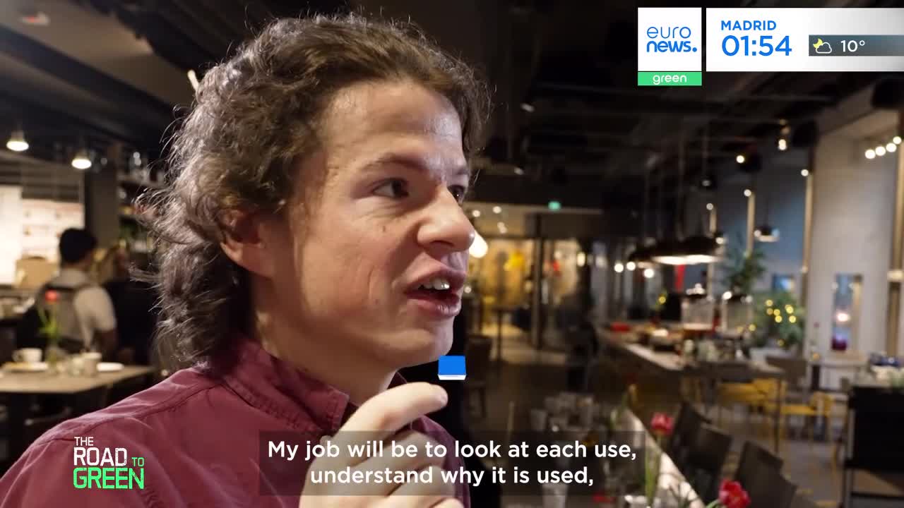 A young man with curly brown hair speaks animatedly, his mouth open as he gestures with his right hand. Behind him, a modern cafe setting unfolds with tables, chairs, and soft lighting, a Euronews overlay indicating Madrid. A young man with curly brown hair speaks animatedly, his mouth open as he gestures with his right hand. Behind him, a modern cafe setting unfolds with tables, chairs, and soft lighting, a Euronews overlay indicating Madrid.