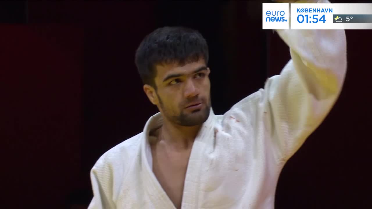 A judoka in a white gi raises his right arm, his gaze fixed. The scoreboard behind him indicates it's 1:54 in Copenhagen, with a temperature of 5 degrees. A judoka in a white gi raises his right arm, his gaze fixed. The scoreboard behind him indicates it's 1:54 in Copenhagen, with a temperature of 5 degrees.