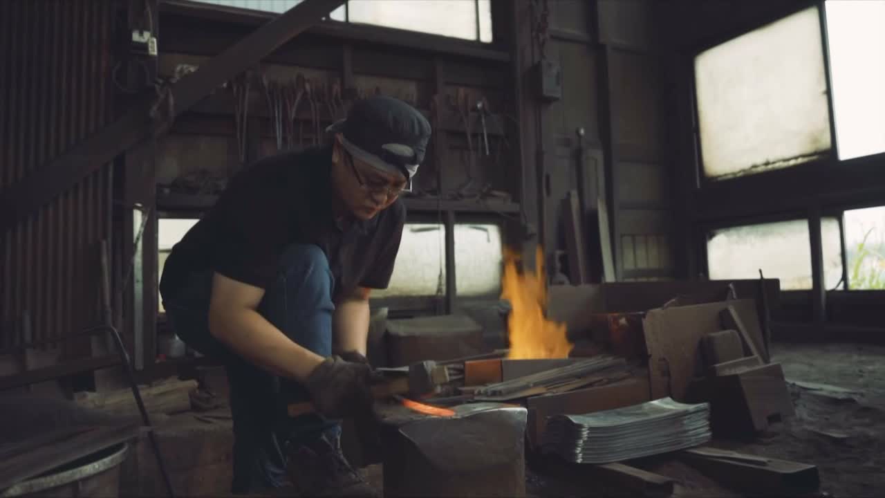 A blacksmith hammers a glowing piece of metal on an anvil. Flames erupt from a forge behind them, illuminating the workshop.