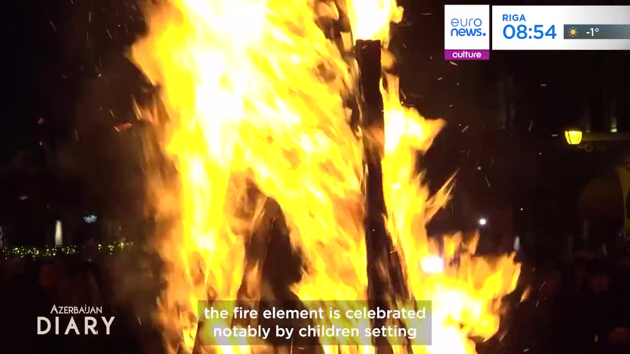 Flames leap high from a bonfire, casting a warm glow on the dark night. Sparks fly upwards, carried by the heat, as people gather around this celebration.