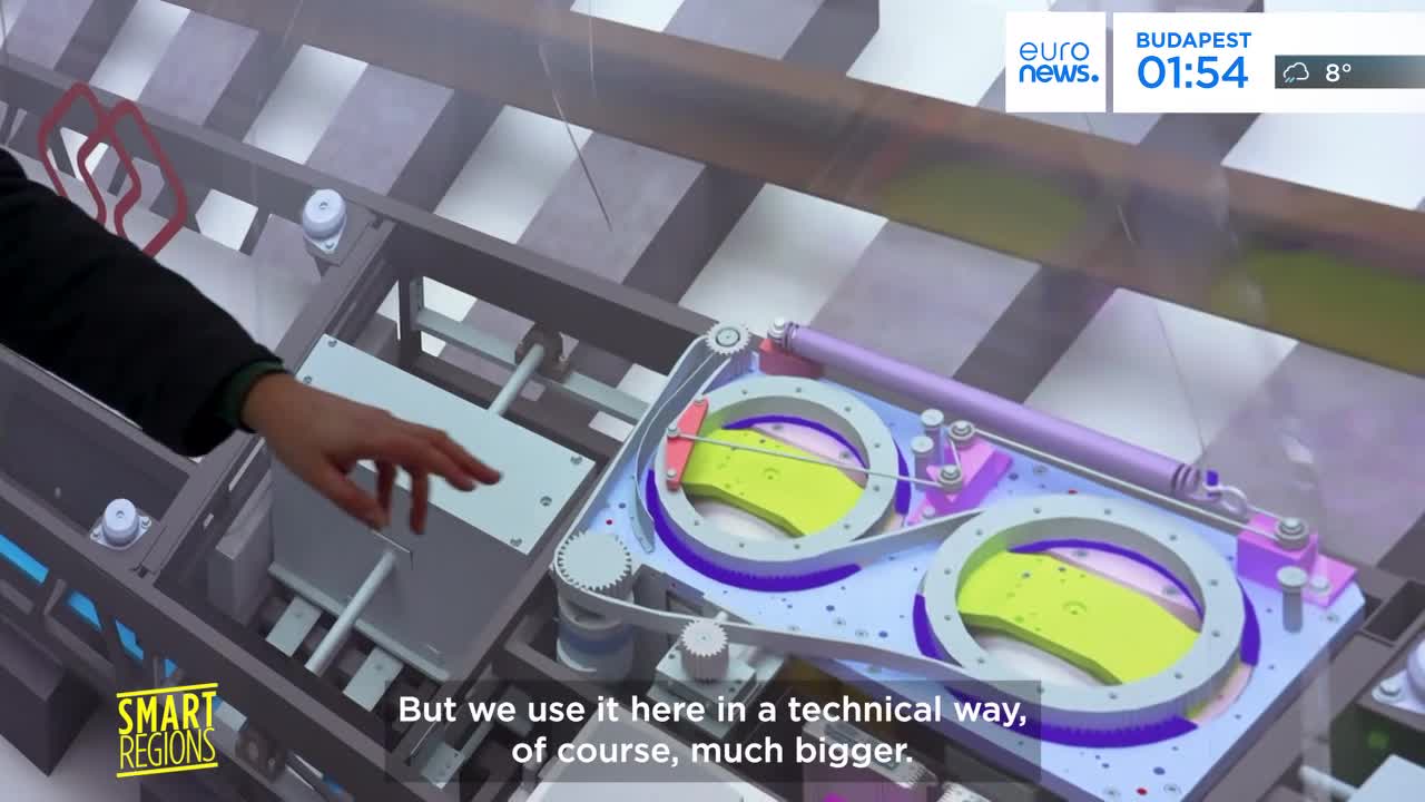 A hand gestures towards a complex, colorful mechanical model. This demonstration, likely part of a French presentation for Euronews, explains a system that's "much bigger" in its real-world application.