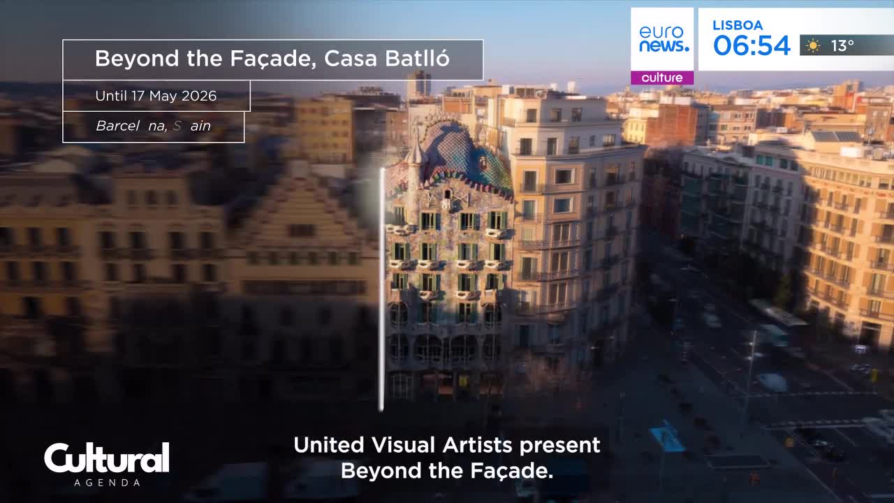 The sun catches the ornate facade of Casa Batlló in Barcelona, a striking building amidst the city's architecture. Below, cars and buses move along the street, their lights streaking as they pass.