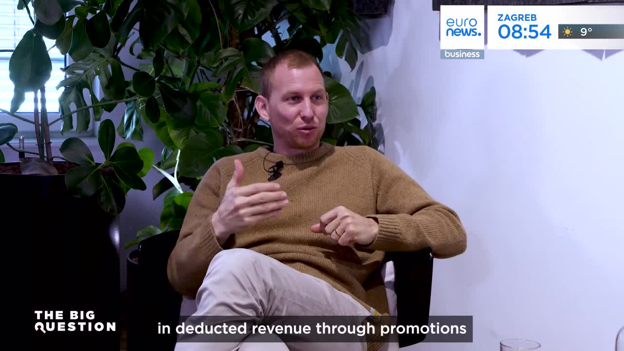 A man in a tan sweater gestures with his hands as he speaks, his face animated. A Euronews graphic in the corner shows the time in Zagreb.