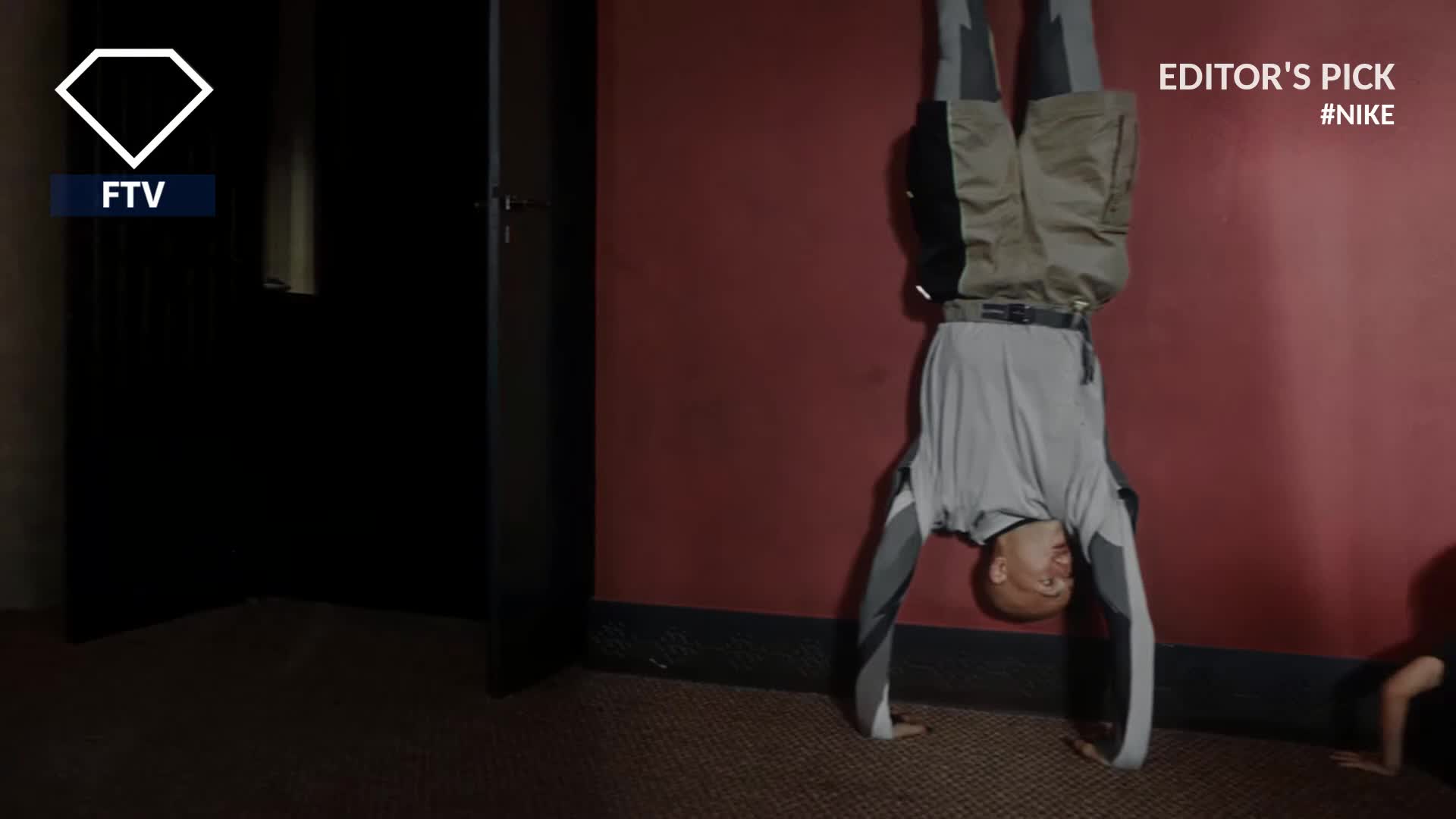 In a room with a red wall, a man in athletic wear balances upside down on his hands. The scene, marked as an Editor's Pick by Nike, is likely a segment for FashionTV Europe.
