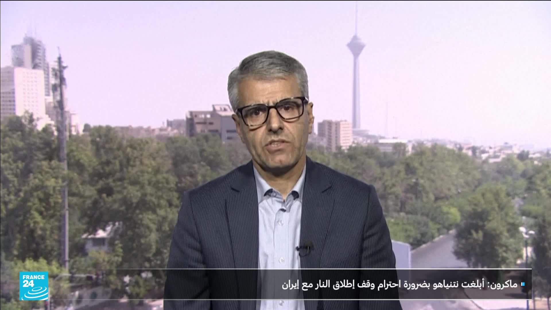 A man in a dark suit and glasses is speaking directly to the camera, with a cityscape visible behind him. The France 24 logo sits in the lower left corner of the screen, and a caption in Arabic is displayed below.
