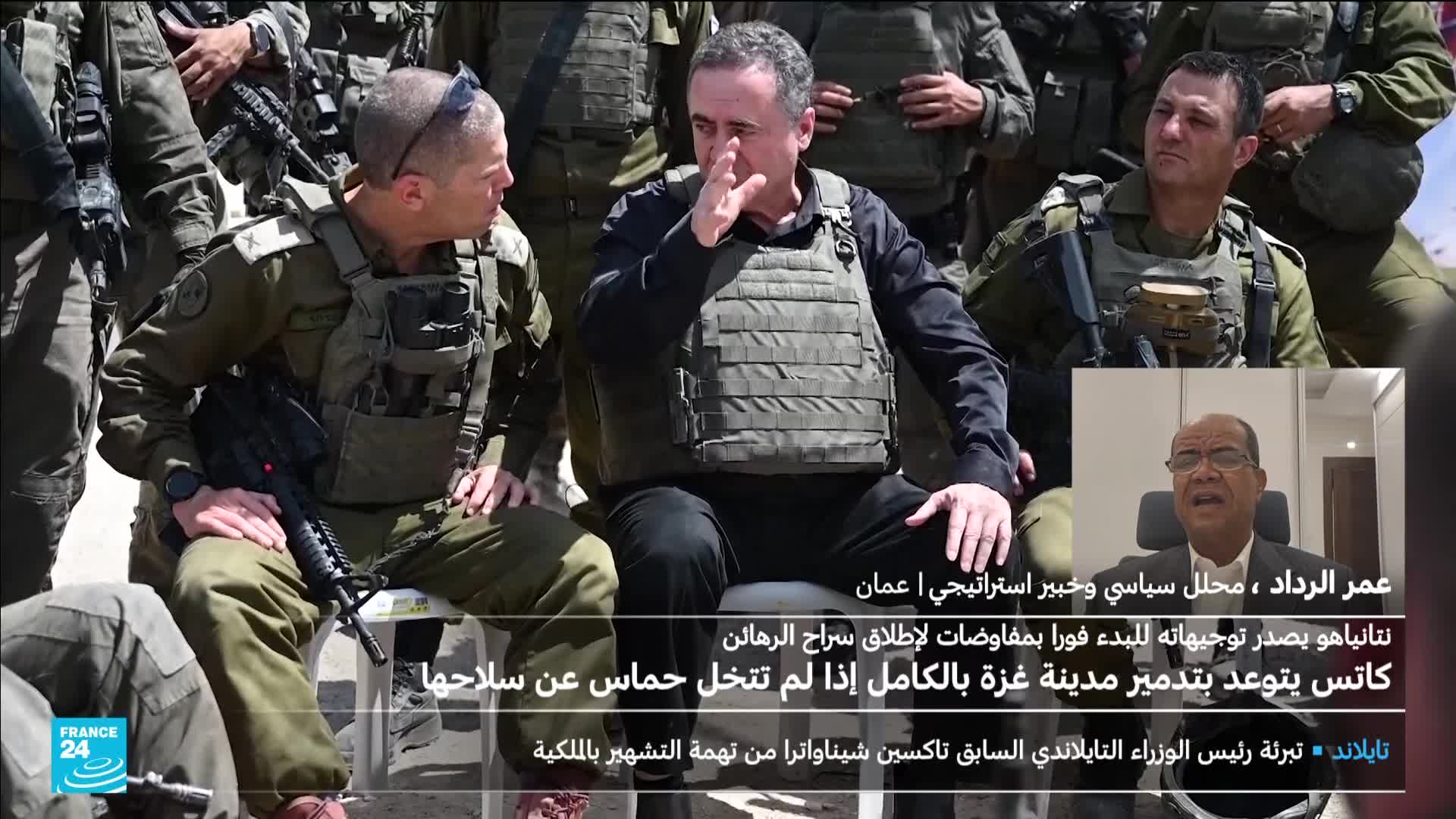 A man in a bulletproof vest gestures with his hand as he sits among soldiers, while a political analyst from Jordan is speaking on France 24. The broadcast is reporting on the threat to destroy Gaza if Hamas doesn't disarm.
