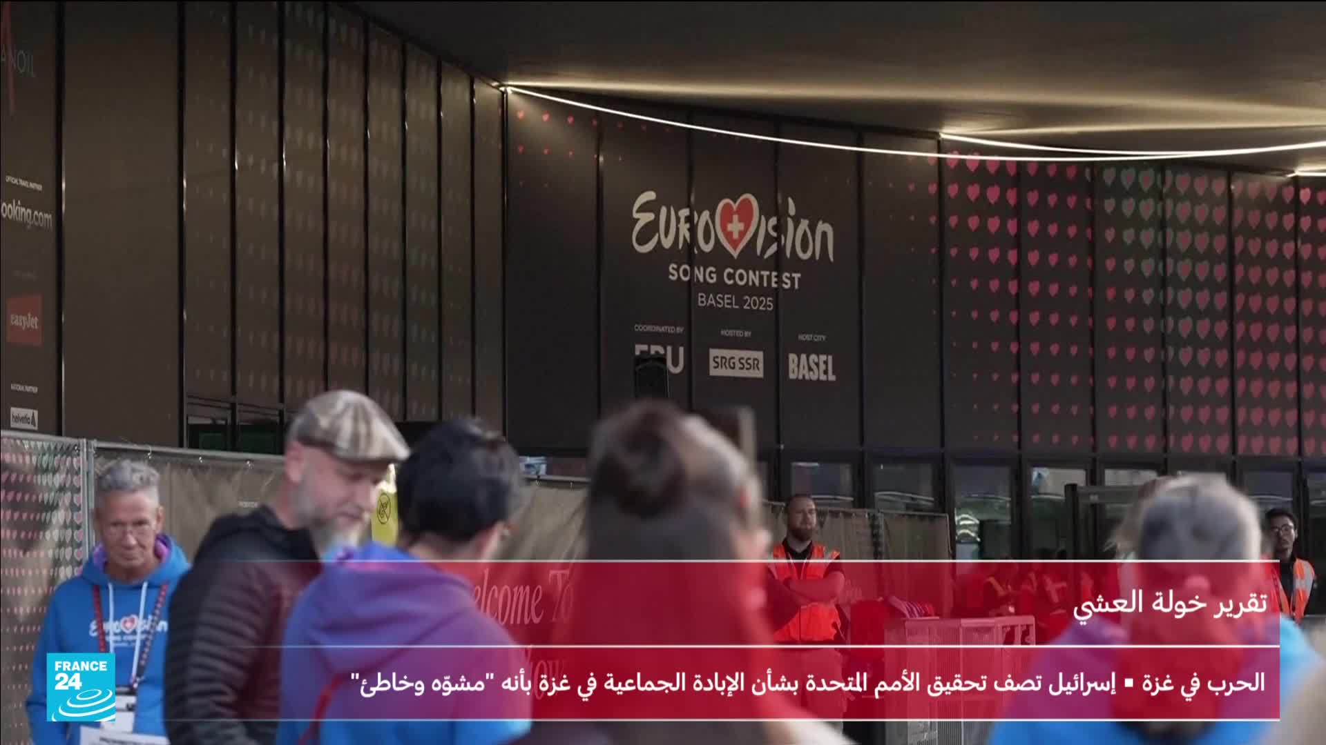 People mill around, some wearing casual clothes, others in what looks like security vests. A large sign for the Eurovision Song Contest in Basel hangs overhead, as reported by France 24.
