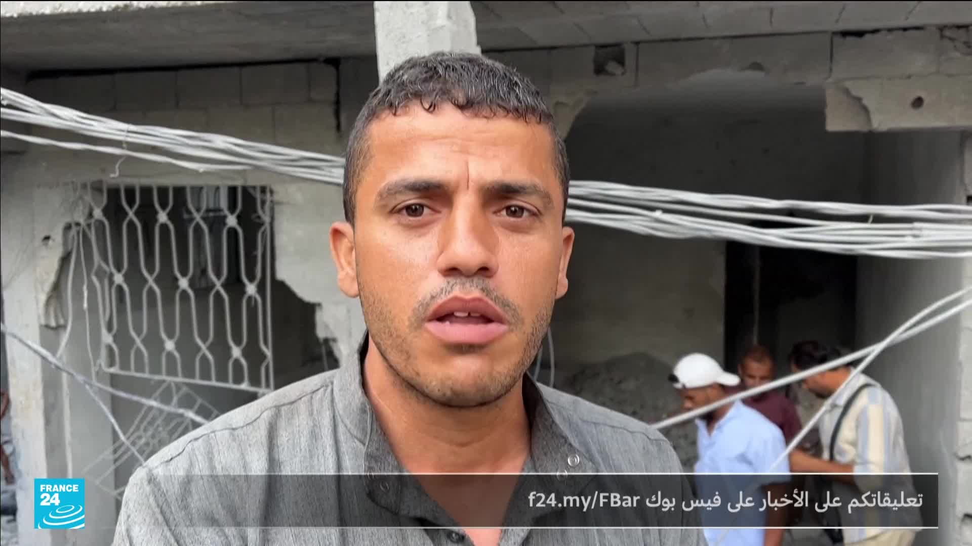 A man, speaking directly to the camera, stands in front of a damaged building. Behind him, a small group of people are gathered, and a France 24 logo is visible in the corner.
