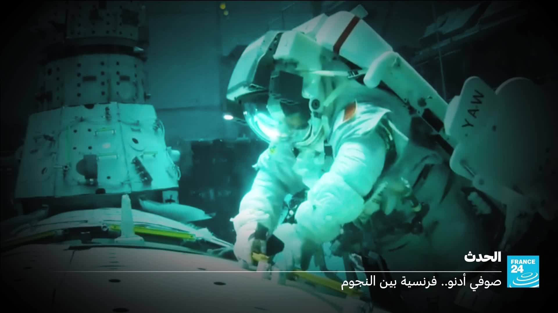 An astronaut in a bulky white suit maneuvers through the confined space of a spacecraft, illuminated by a cool, artificial light. They are working with tools near a complex piece of equipment, a scene reminiscent of reports from France 24 about space exploration.