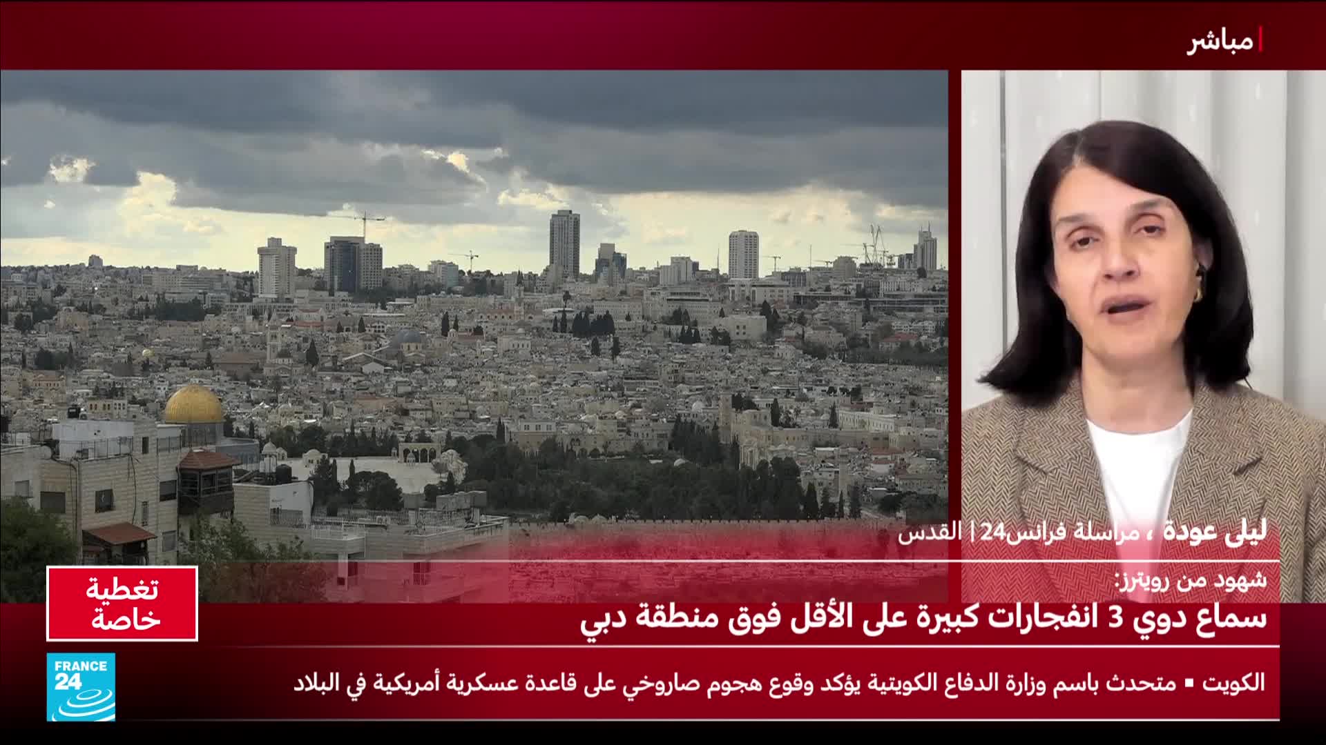 A woman speaks from a studio, her image split-screened with a wide view of a dense, historic city under a cloudy sky. The city's buildings, a mix of stone structures and modern high-rises, stretch across the landscape.