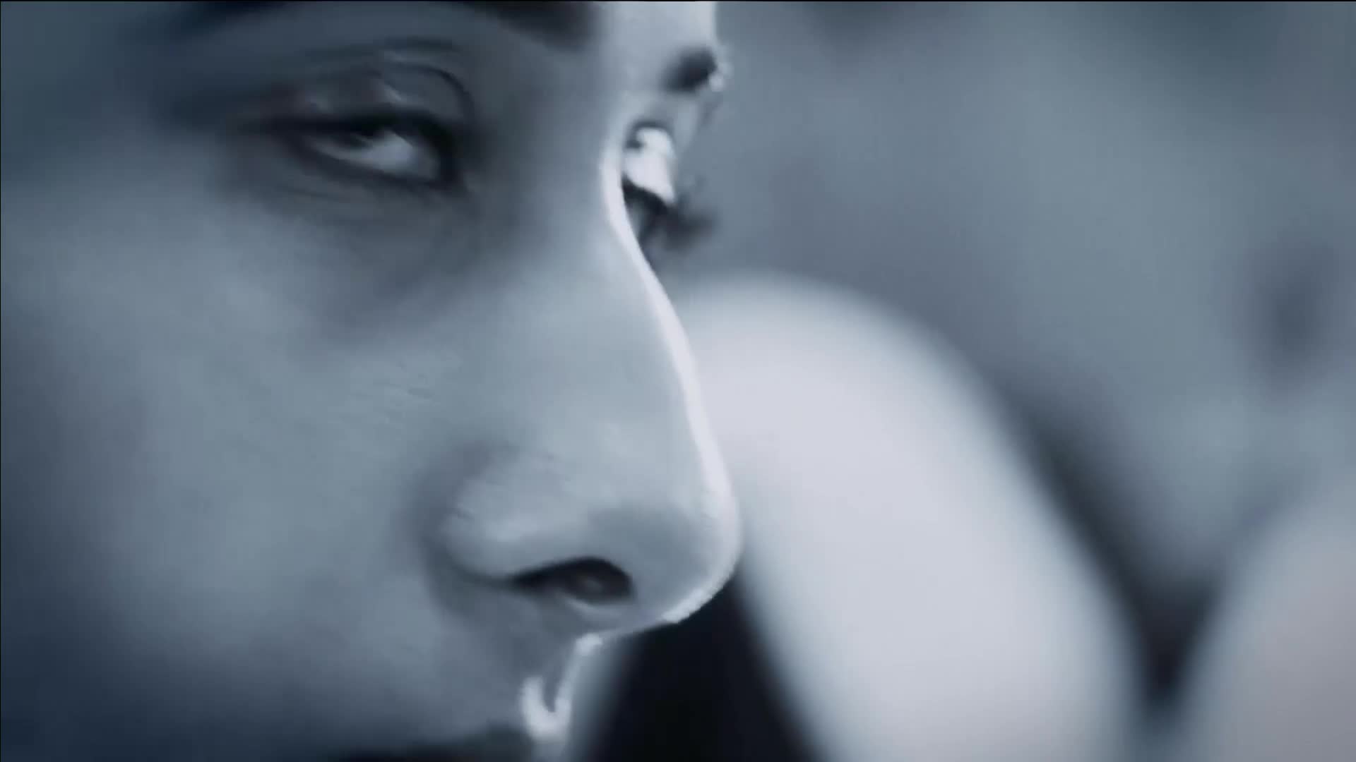 A woman's face, captured in a close-up, shows her eye looking intently to the side. A single tear glistens on her cheek, reflecting the dim light.