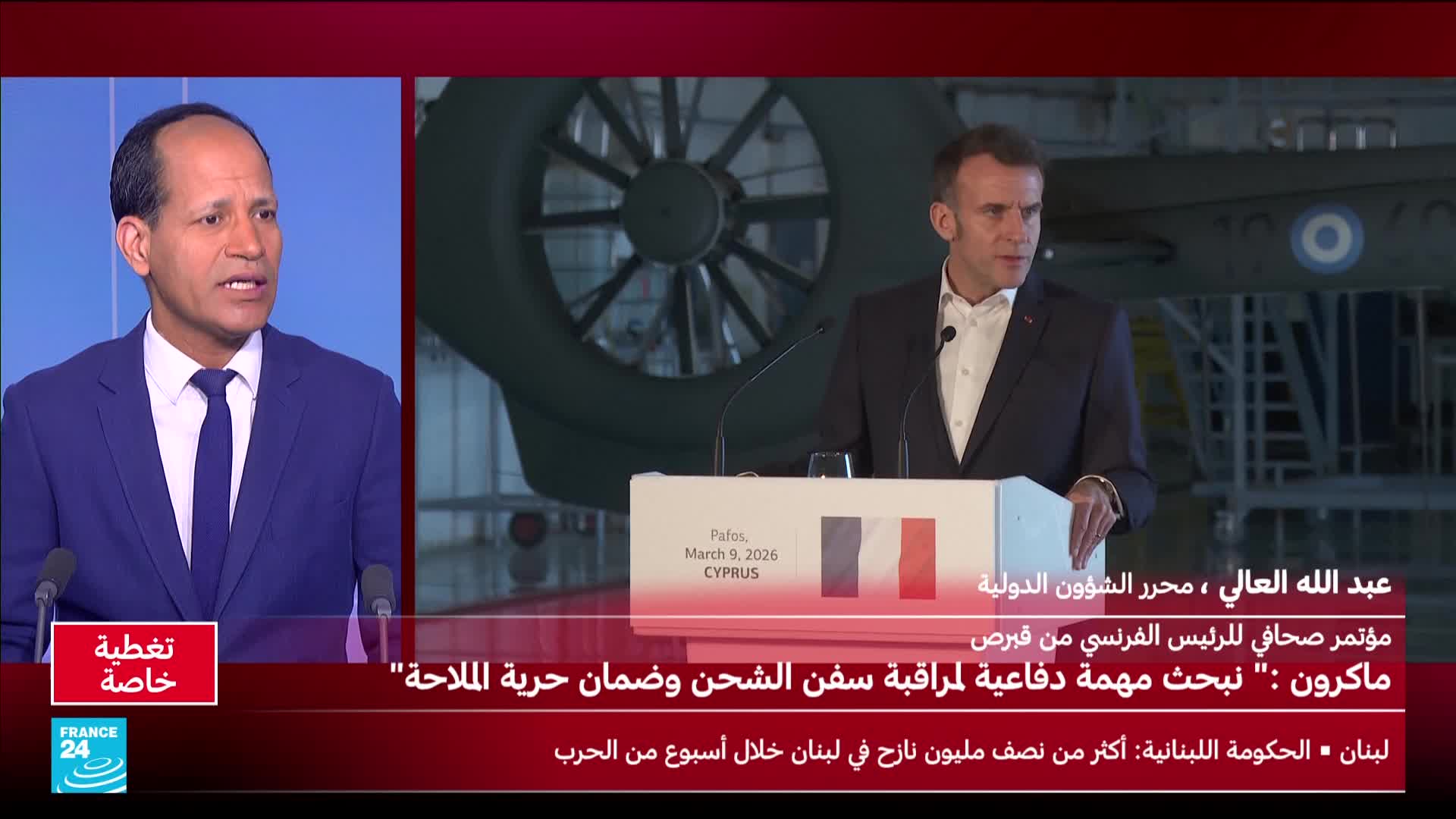 Emmanuel Macron stands at a podium, speaking to an audience. Behind him, a large, dark helicopter rotor is visible.