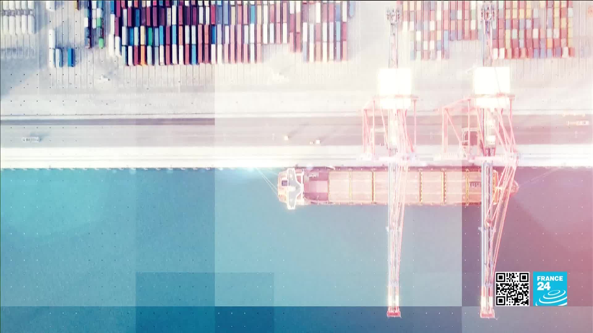 A large cargo ship is docked, its containers being lifted by towering red cranes. Rows of stacked containers stretch across the quay behind it.