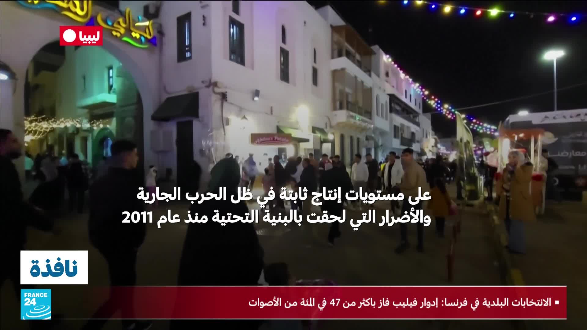 A crowd gathers on a street decorated with colorful lights, people are walking and talking. A truck with a large banner is parked on the right side of the street, and a group of people are gathered around it. A crowd gathers on a street decorated with colorful lights, people are walking and talking. A truck with a large banner is parked on the right side of the street, and a group of people are gathered around it.