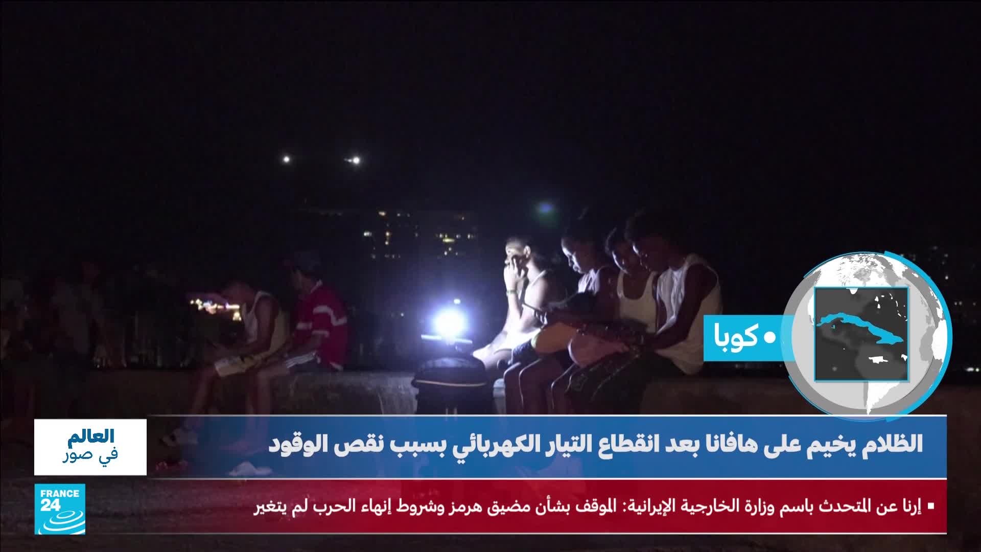 A group of people sit in the dark, illuminated by a single bright lantern. Distant lights twinkle on a hillside, suggesting a city or town struggling with power outages. A group of people sit in the dark, illuminated by a single bright lantern. Distant lights twinkle on a hillside, suggesting a city or town struggling with power outages.