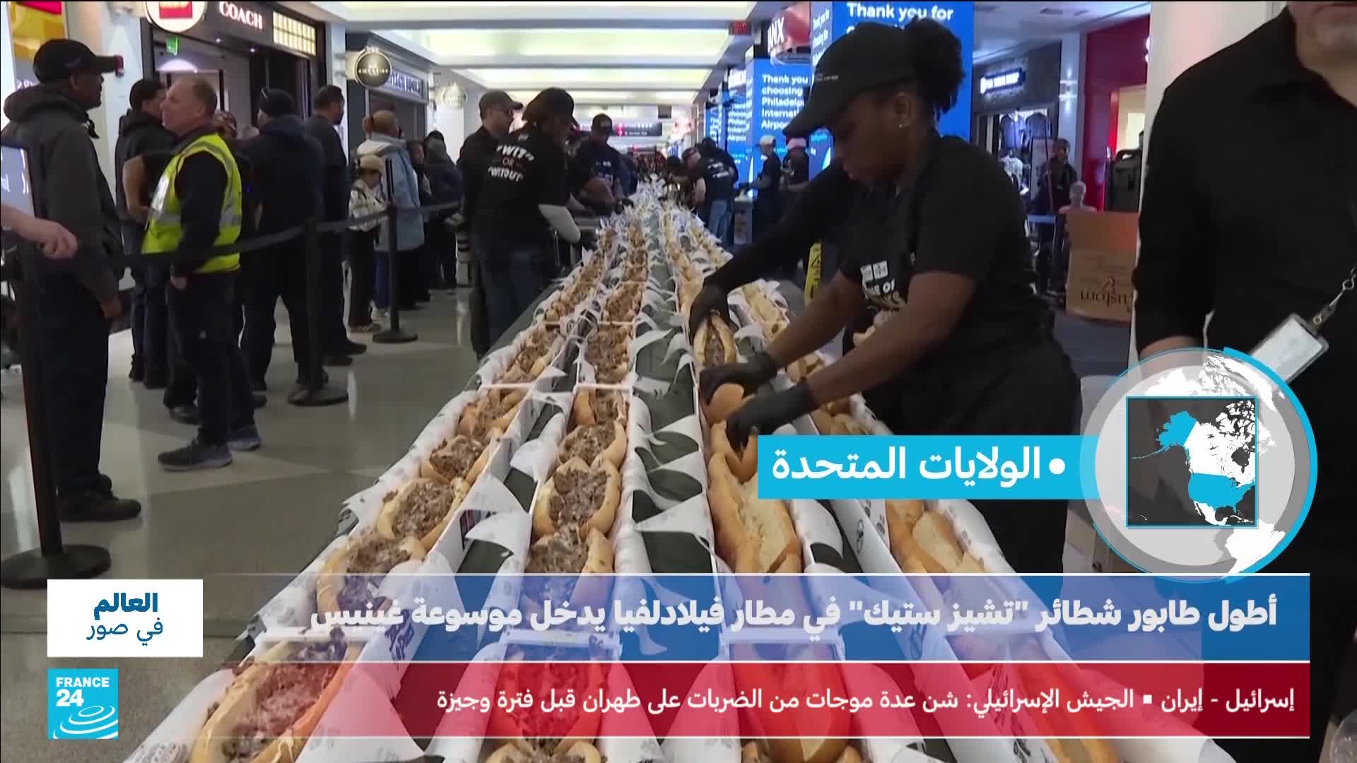 A long line of people stretches into the distance, waiting for what looks like a record-breaking sandwich. Workers in black shirts and gloves are busy assembling them on a long table. A long line of people stretches into the distance, waiting for what looks like a record-breaking sandwich. Workers in black shirts and gloves are busy assembling them on a long table.