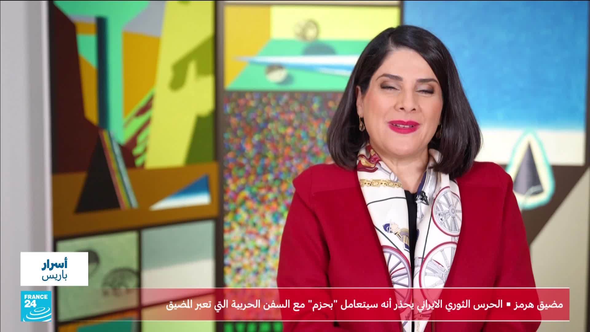 A woman in a red coat and patterned scarf speaks directly to the camera. Behind her, abstract paintings fill the background, with a France 24 logo visible in the lower left corner.