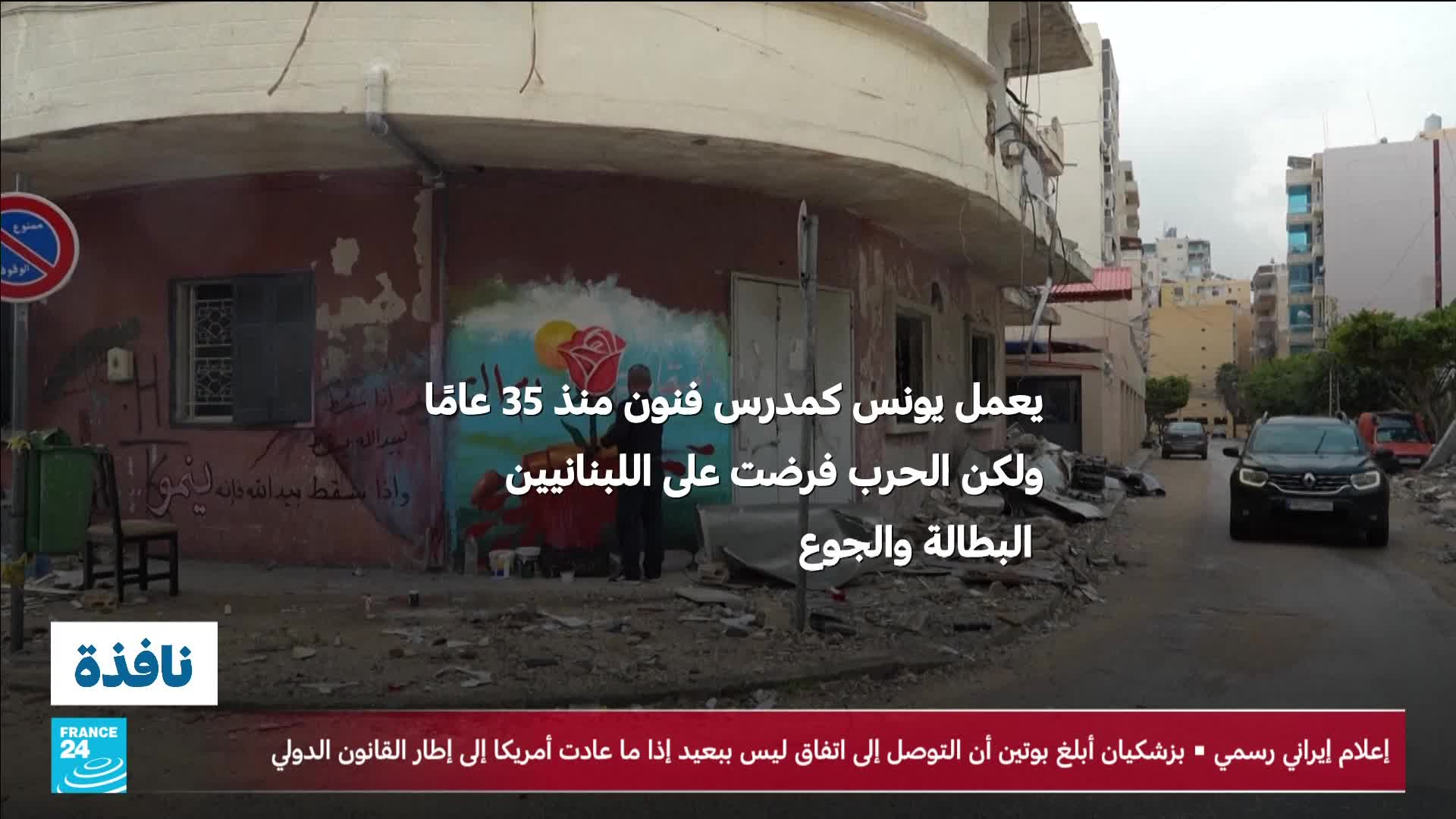 A dark SUV drives down a debris-strewn street in a city. The building to the left has a mural of a rose and sun, with Arabic text overlaying it.