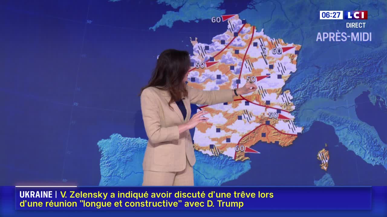 A woman in a beige suit gestures toward a map of France, pointing out weather patterns on the LCI broadcast. The screen displays a forecast with red lines and numbers, indicating wind speeds and potential weather conditions.
