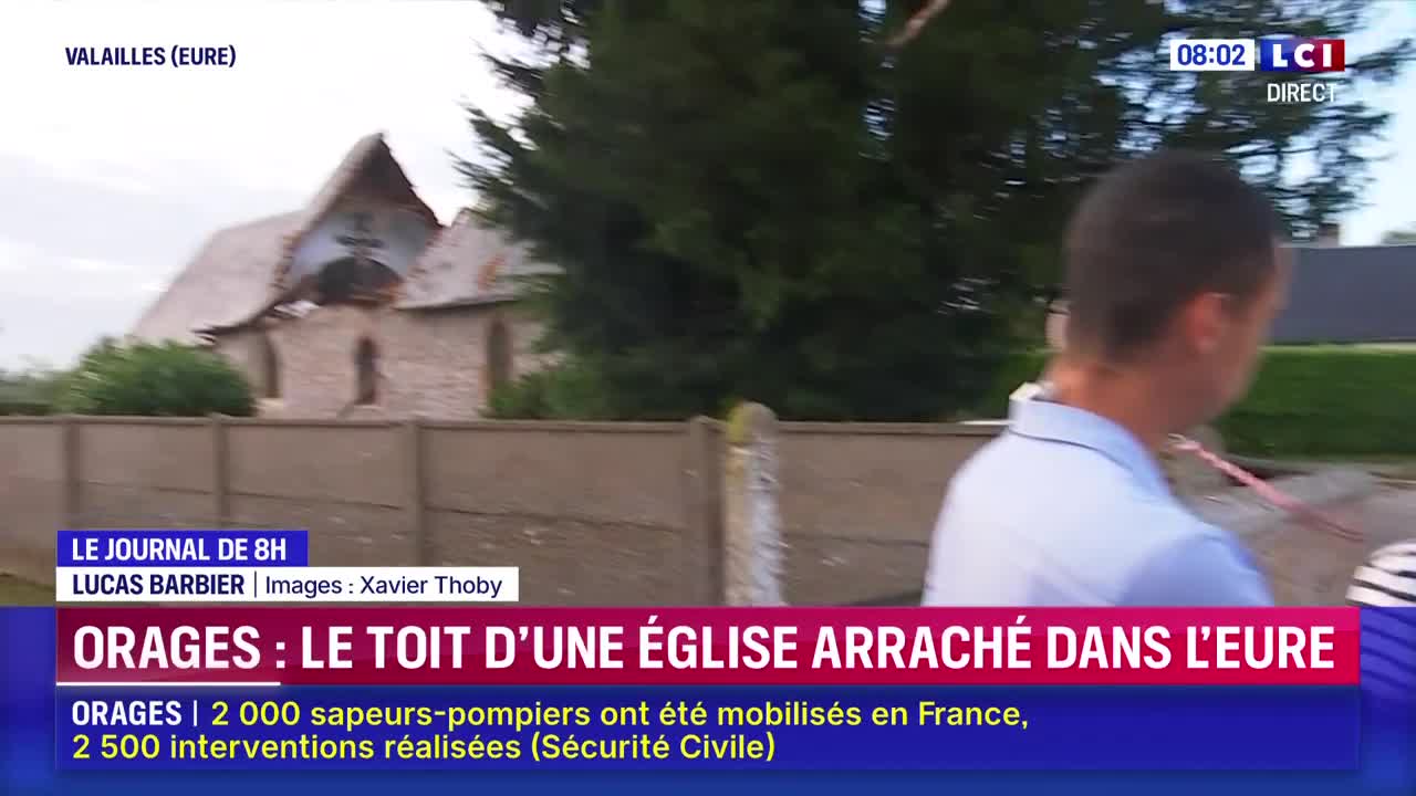 A man in a light blue shirt walks past the camera, the damaged roof of a church visible behind him. The LCI logo in the upper right corner signals a live broadcast from the Eure region of France.
