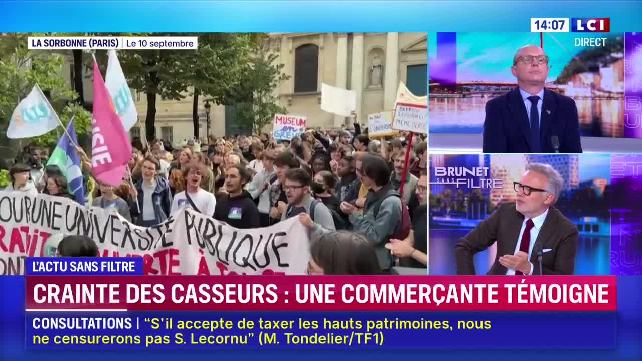 A crowd of people, some carrying banners and flags, marches down a street in front of a building. The scene is being broadcast on LCI, with commentators discussing the event.
