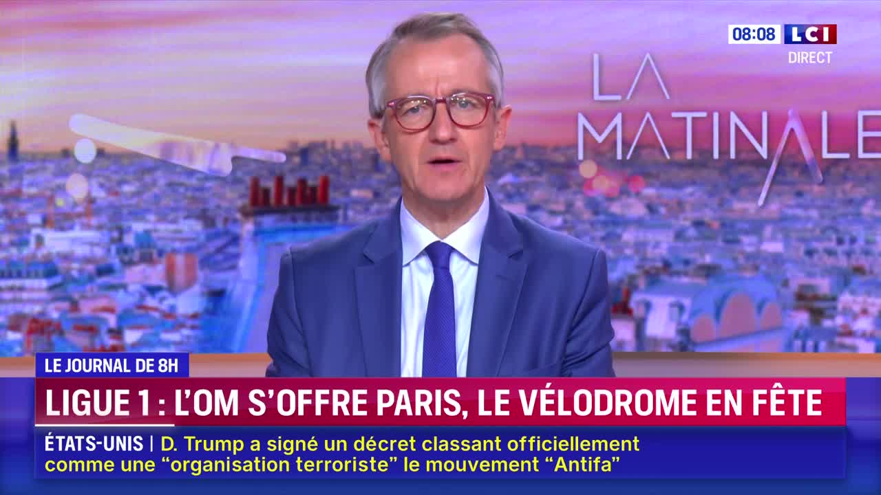 A man in a blue suit and glasses is speaking directly to the camera, framed by a cityscape backdrop. The LCI logo and "La Matinale" are visible, along with news headlines in French.

