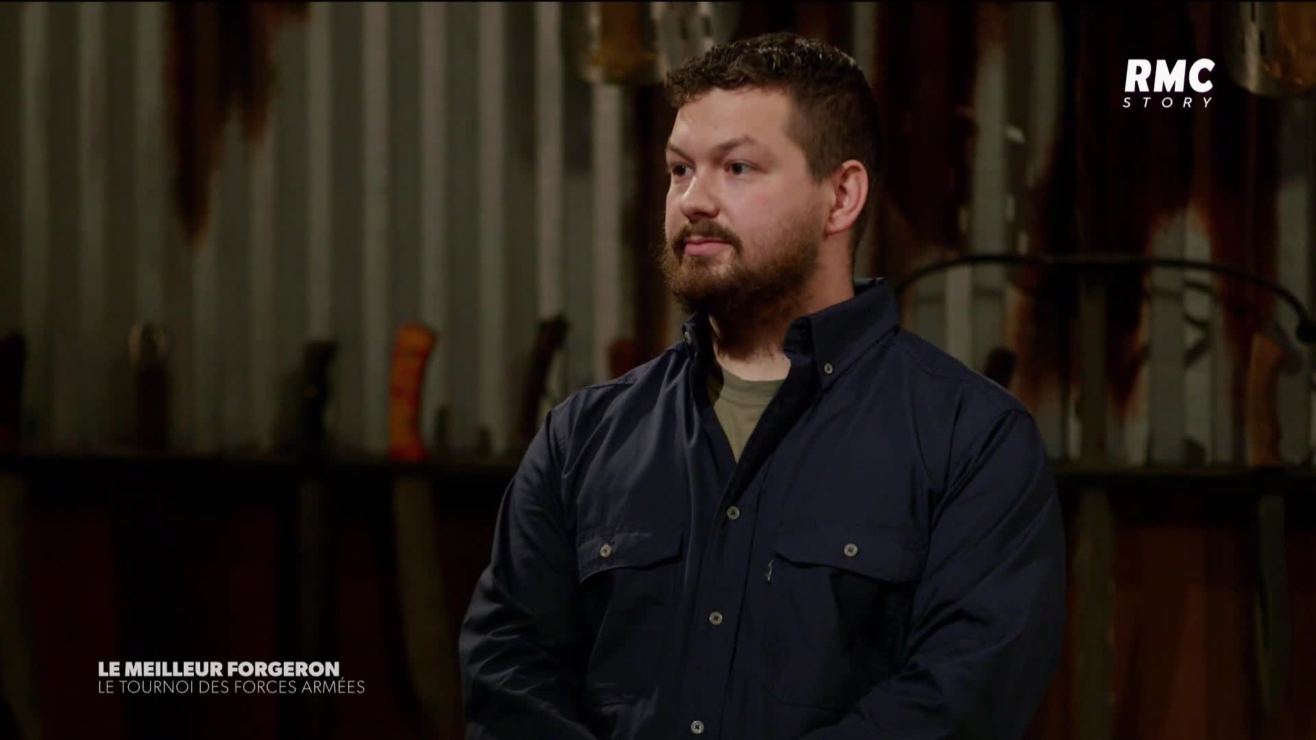 The man is standing still, looking off to the side in a workshop. Behind him, the RMC Story logo sits above a backdrop of tools and equipment.
